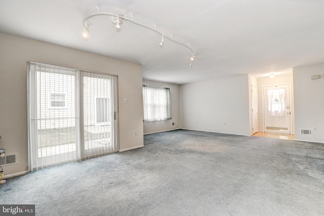 unfurnished living room featuring rail lighting, visible vents, and carpet floors