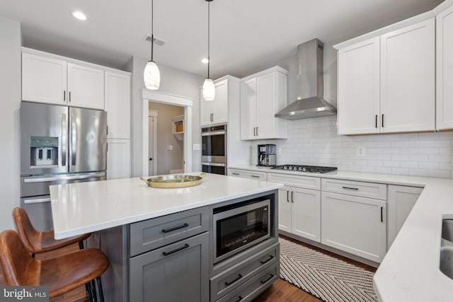 kitchen with stainless steel appliances, backsplash, light countertops, and wall chimney range hood