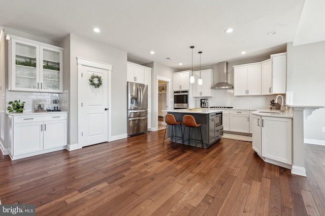 kitchen with a breakfast bar, stainless steel fridge with ice dispenser, a sink, white cabinetry, and wall chimney range hood