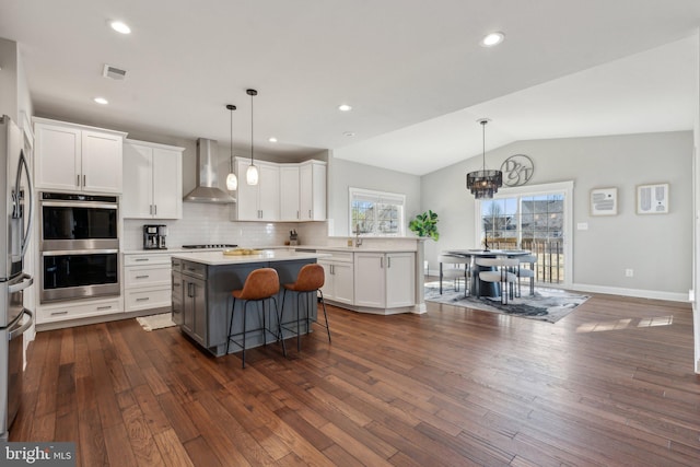 kitchen featuring backsplash, a kitchen island, appliances with stainless steel finishes, white cabinetry, and wall chimney exhaust hood