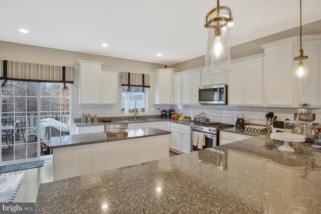 kitchen featuring stainless steel appliances, decorative backsplash, white cabinetry, a sink, and dark stone countertops