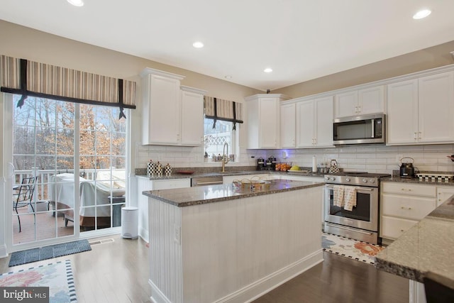 kitchen featuring white cabinets, appliances with stainless steel finishes, dark stone counters, and wood finished floors