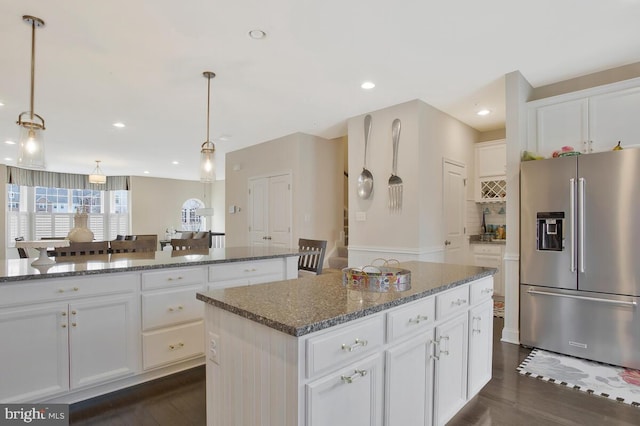 kitchen with dark wood-style flooring, stainless steel refrigerator with ice dispenser, white cabinetry, a kitchen island, and dark stone countertops