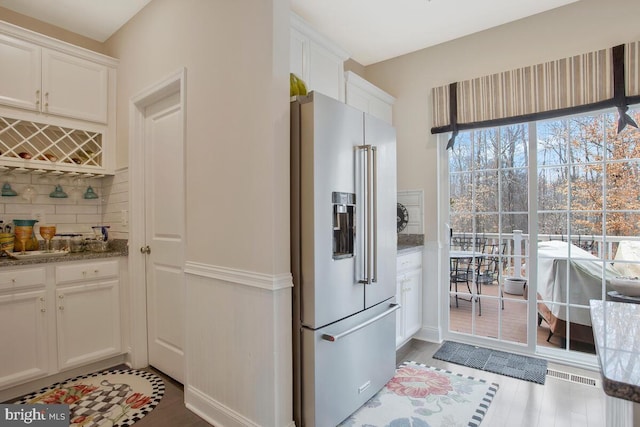 kitchen with high end refrigerator, light stone countertops, white cabinetry, and decorative backsplash