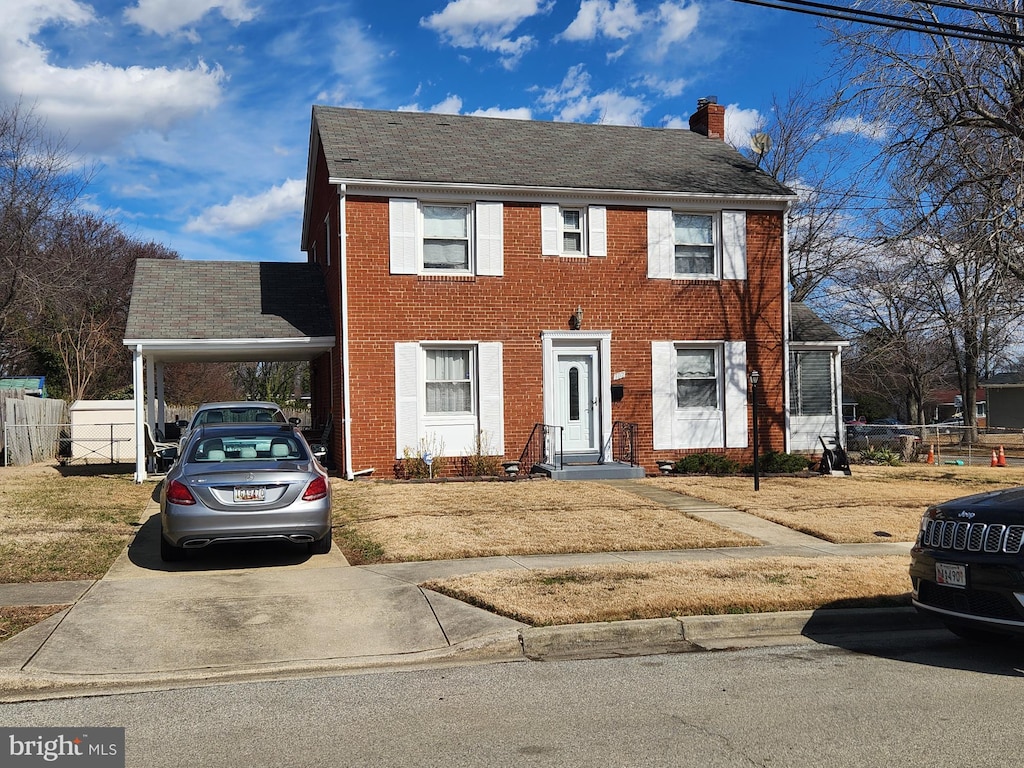 colonial house with an attached carport, fence, roof with shingles, brick siding, and a chimney