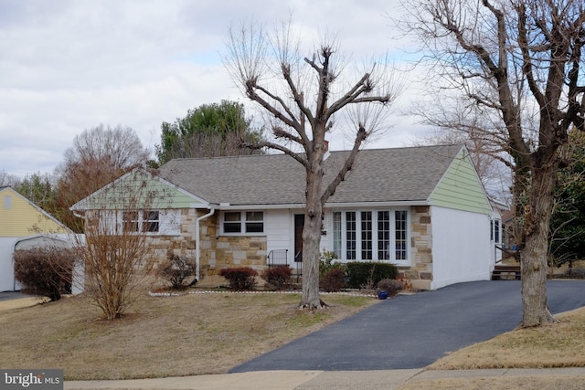 ranch-style home featuring a shingled roof, stone siding, driveway, and a front lawn