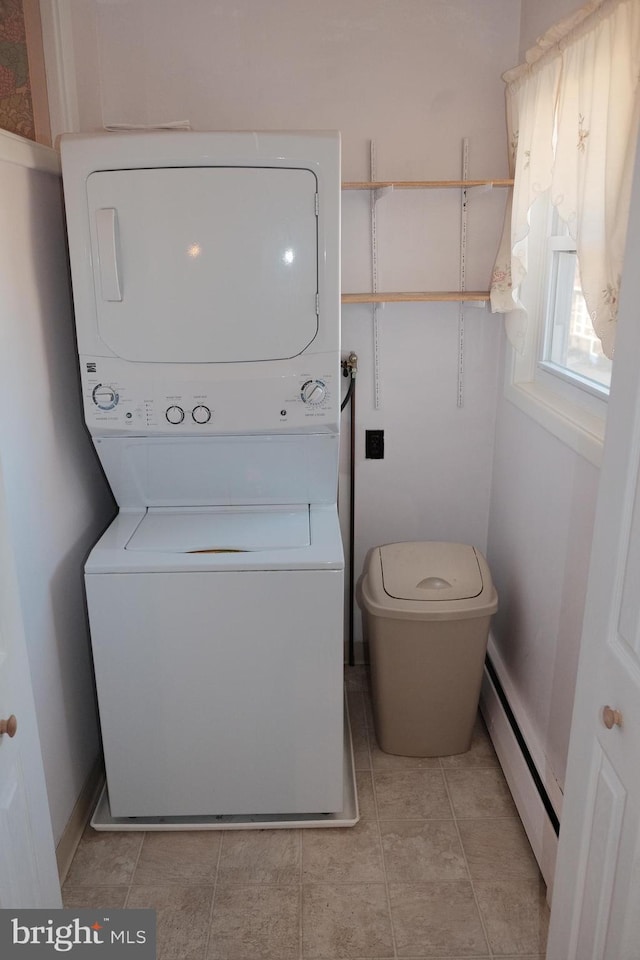 clothes washing area featuring light tile patterned floors, a baseboard radiator, stacked washing maching and dryer, laundry area, and baseboards