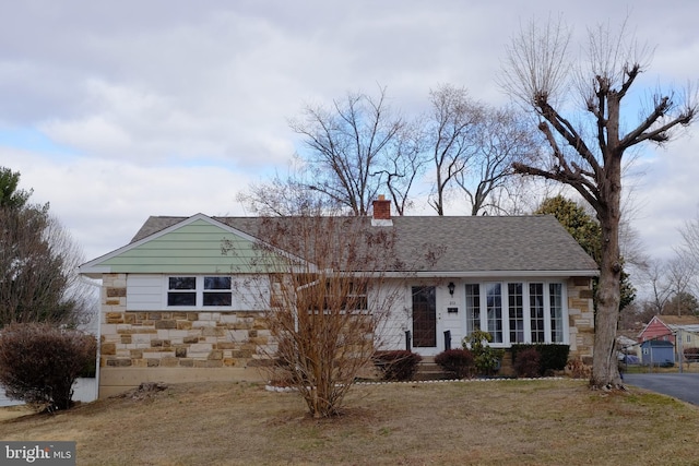 view of front facade featuring stone siding, a shingled roof, a chimney, and a front lawn