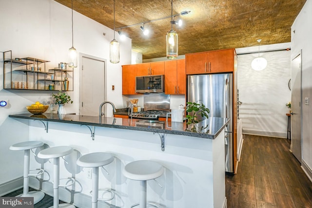 kitchen featuring brown cabinets, dark wood finished floors, decorative light fixtures, appliances with stainless steel finishes, and dark stone counters