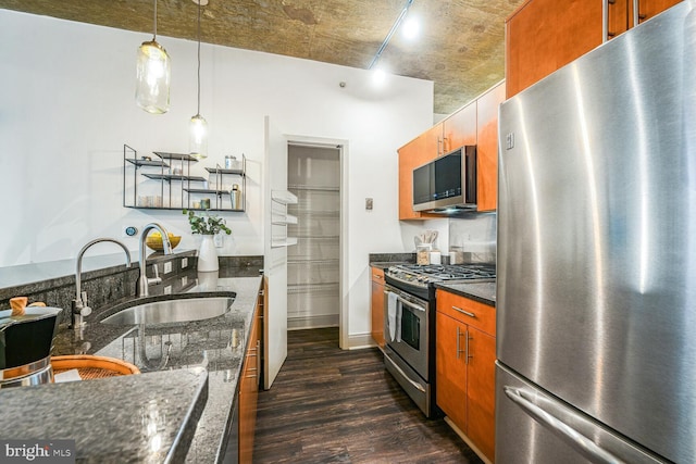 kitchen featuring brown cabinets, dark stone countertops, dark wood-style flooring, stainless steel appliances, and a sink