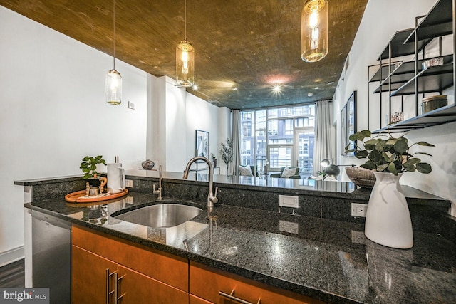 kitchen featuring pendant lighting, stainless steel dishwasher, open floor plan, a sink, and dark stone countertops