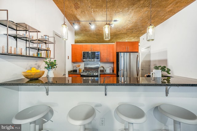 kitchen with a peninsula, appliances with stainless steel finishes, brown cabinetry, and pendant lighting