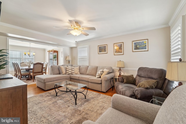 living area with ceiling fan with notable chandelier, wood finished floors, and ornamental molding