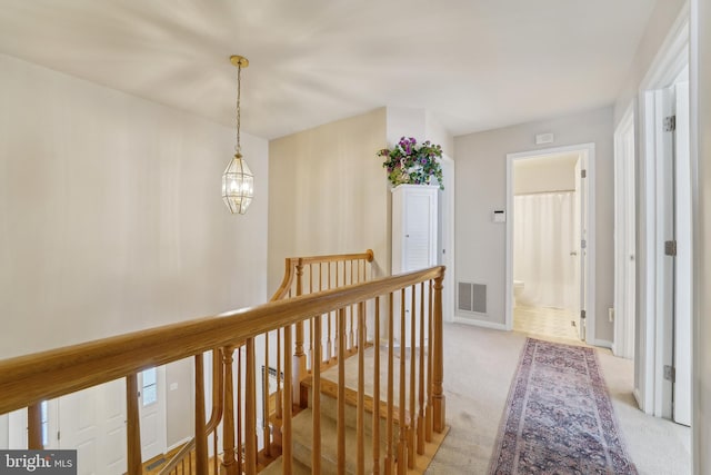 hallway featuring baseboards, visible vents, light carpet, an upstairs landing, and a chandelier