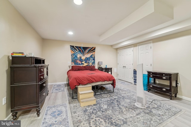 bedroom with a tray ceiling, light wood-style flooring, recessed lighting, and baseboards