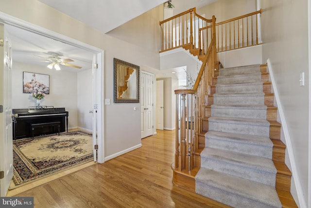 stairs featuring wood finished floors, baseboards, a towering ceiling, and ceiling fan