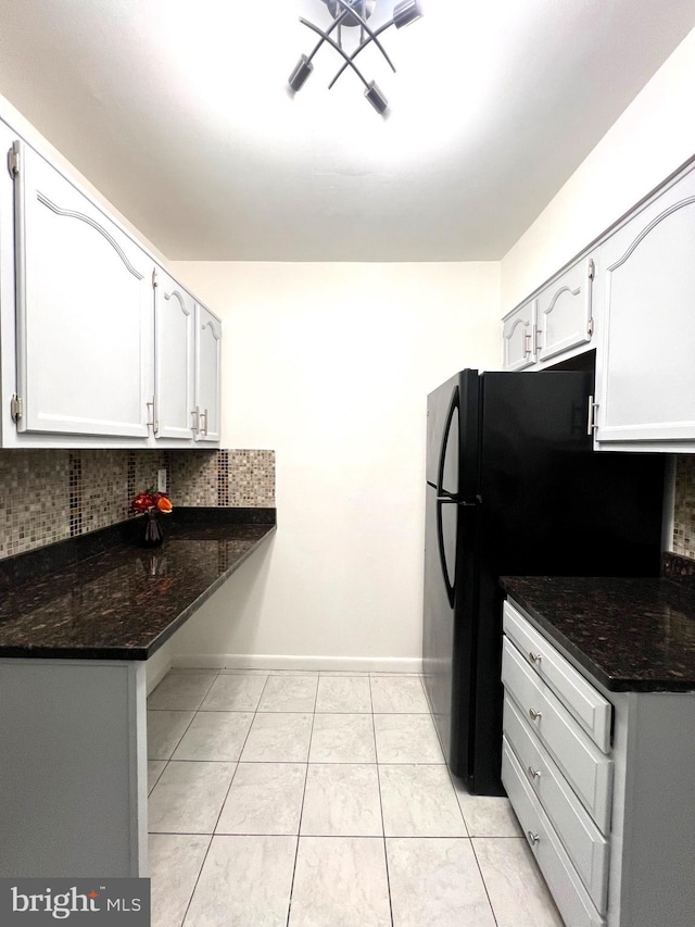 kitchen featuring tasteful backsplash, white cabinets, dark stone countertops, freestanding refrigerator, and light tile patterned flooring