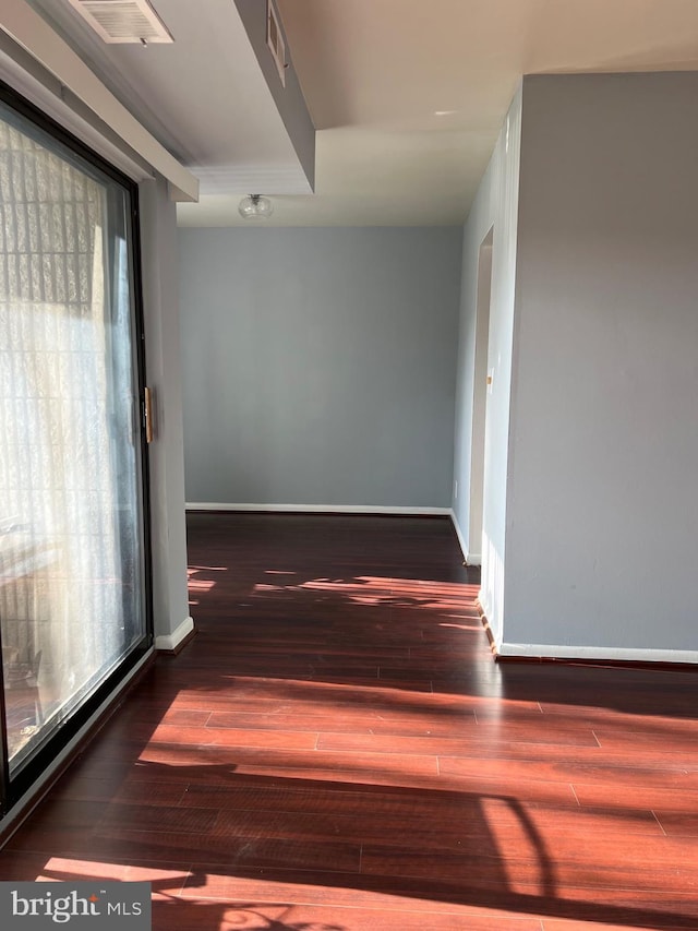 hallway with baseboards, visible vents, and wood finished floors