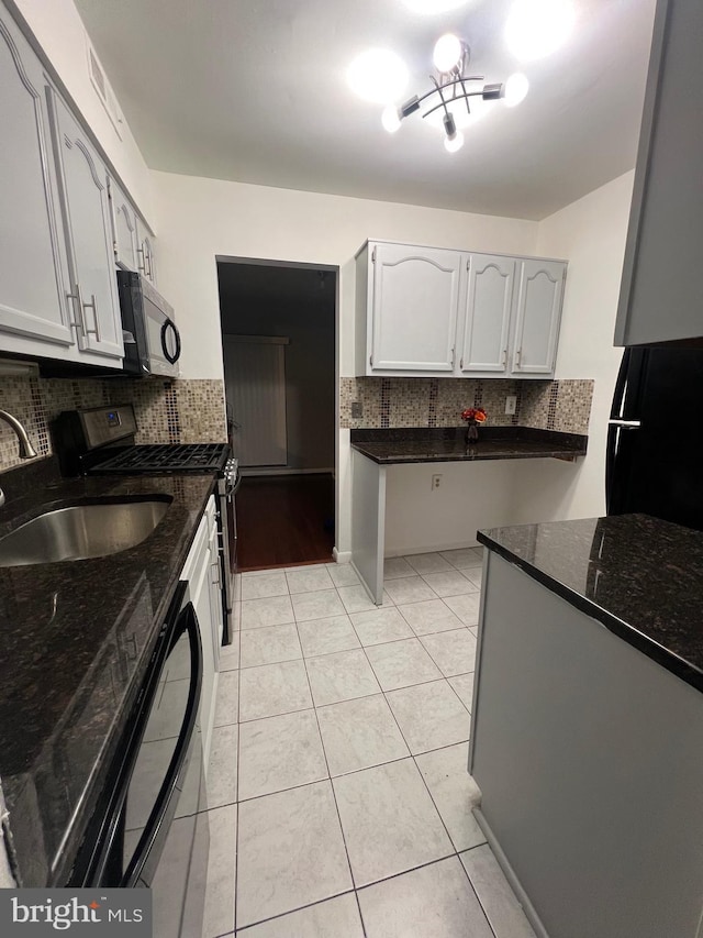 kitchen featuring light tile patterned floors, a sink, appliances with stainless steel finishes, backsplash, and dark stone countertops