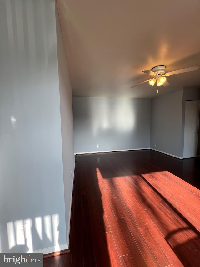 unfurnished room with a ceiling fan, dark wood-style flooring, and baseboards