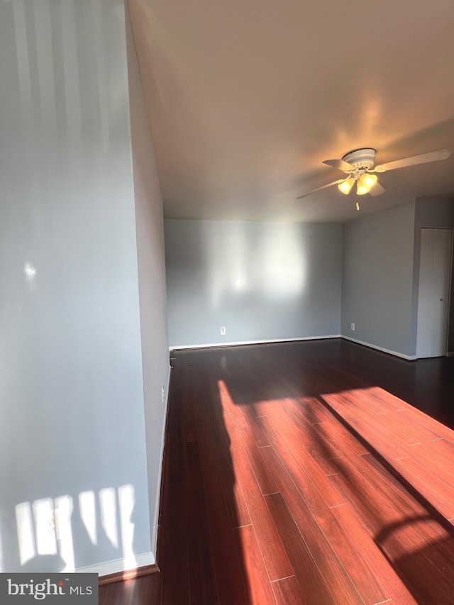 spare room with dark wood finished floors, a ceiling fan, and baseboards