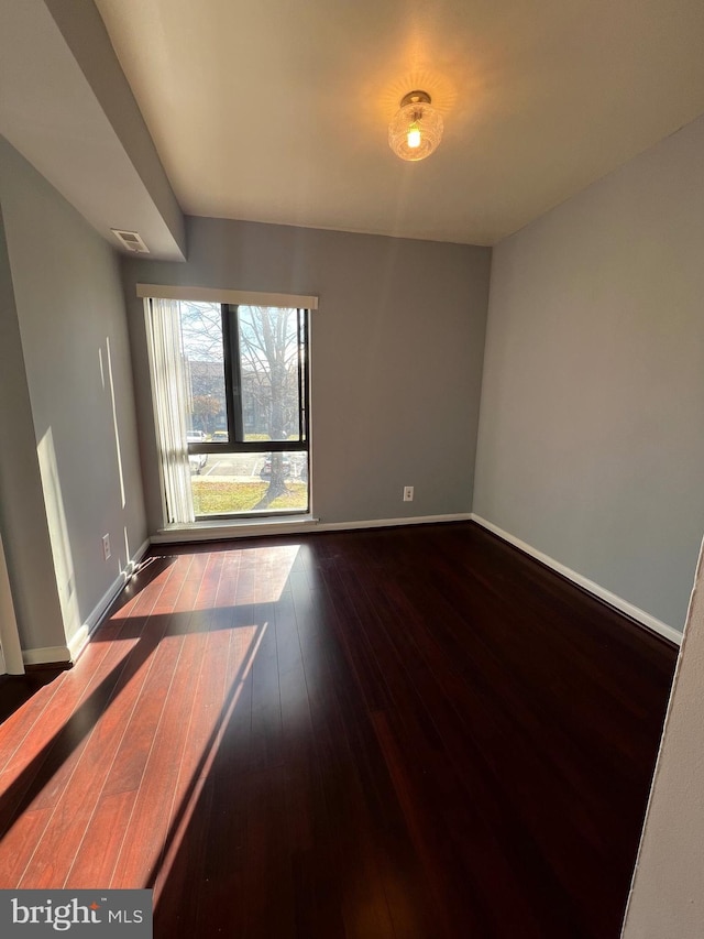 empty room with dark wood finished floors, visible vents, and baseboards