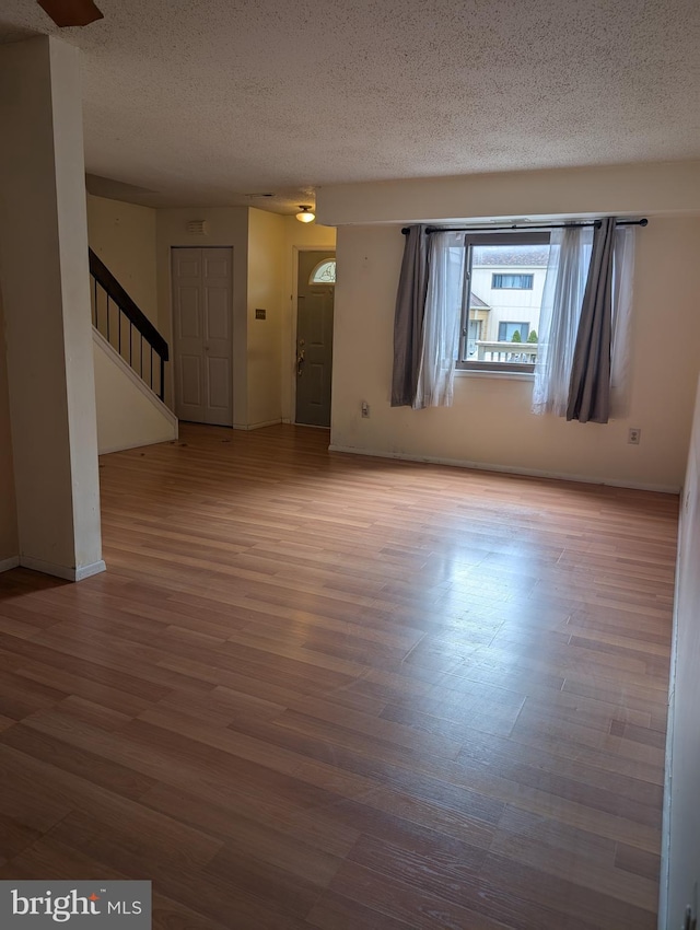 unfurnished room with baseboards, stairway, a textured ceiling, and wood finished floors