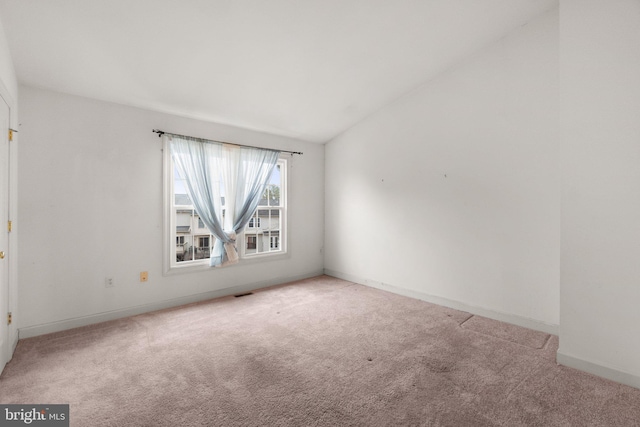 carpeted spare room featuring baseboards, visible vents, and vaulted ceiling