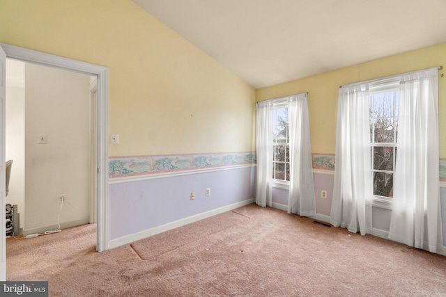 spare room with lofted ceiling, carpet flooring, visible vents, baseboards, and wainscoting