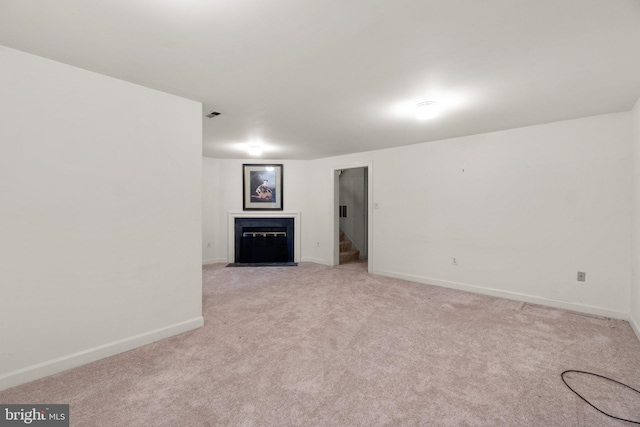 unfurnished living room featuring baseboards, visible vents, light colored carpet, a fireplace with flush hearth, and stairs