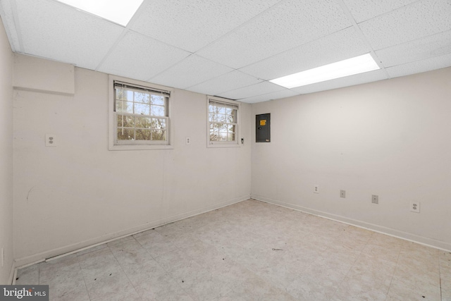 below grade area featuring baseboards, light floors, a paneled ceiling, and electric panel