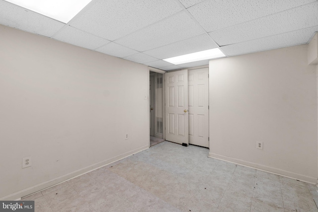 finished basement featuring baseboards, a drop ceiling, and tile patterned floors