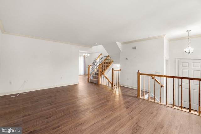 unfurnished living room with a chandelier, ornamental molding, wood finished floors, and baseboards