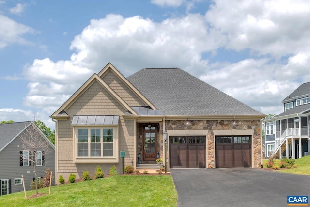 craftsman house featuring driveway, stone siding, an attached garage, a standing seam roof, and a front lawn