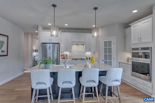 kitchen with light wood finished floors, appliances with stainless steel finishes, a center island with sink, and decorative backsplash