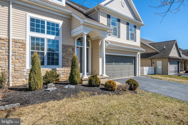 view of front of property with fence, roof with shingles, a garage, stone siding, and driveway