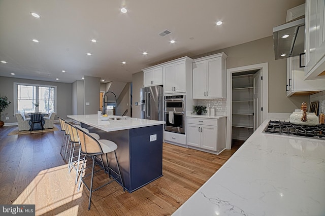 kitchen with stainless steel appliances, a sink, white cabinetry, visible vents, and decorative backsplash