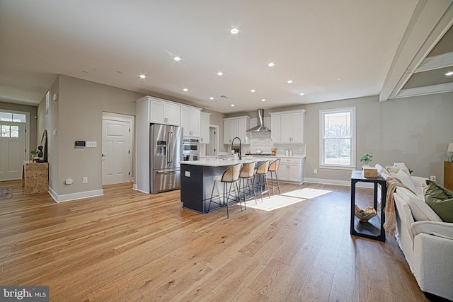 kitchen with light wood finished floors, stainless steel fridge with ice dispenser, wall chimney exhaust hood, open floor plan, and a kitchen bar