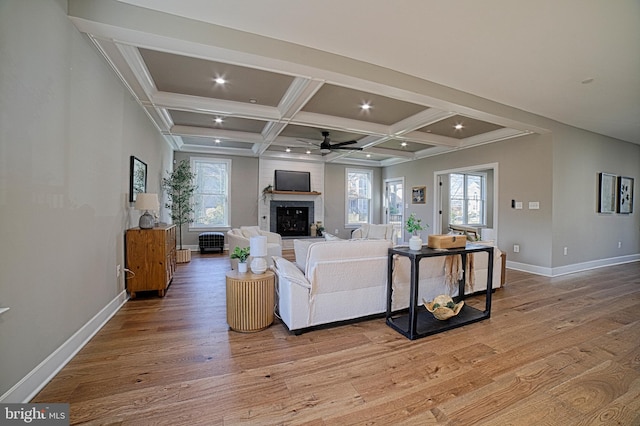 living room featuring a fireplace, light wood-style floors, ceiling fan, coffered ceiling, and baseboards