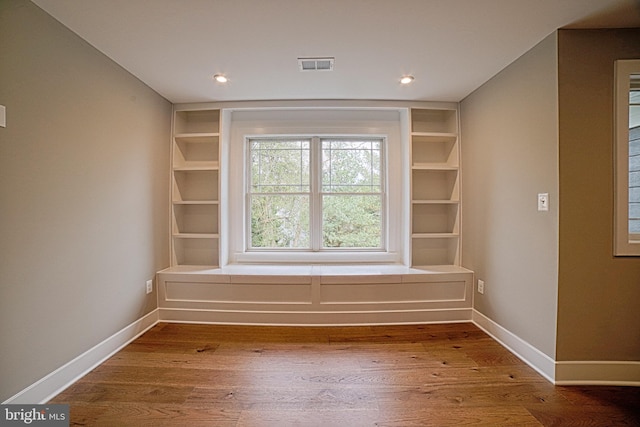 empty room with built in shelves, visible vents, baseboards, and wood finished floors