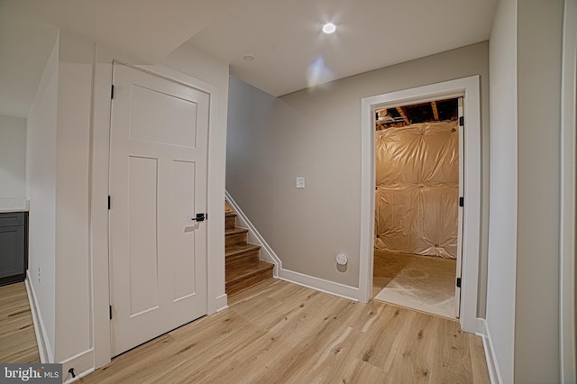 corridor with light wood finished floors, stairway, and baseboards