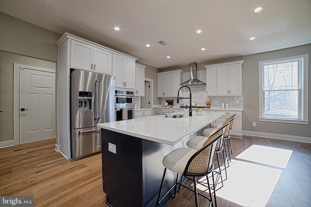 kitchen with light wood-style flooring, stainless steel appliances, white cabinetry, wall chimney exhaust hood, and tasteful backsplash