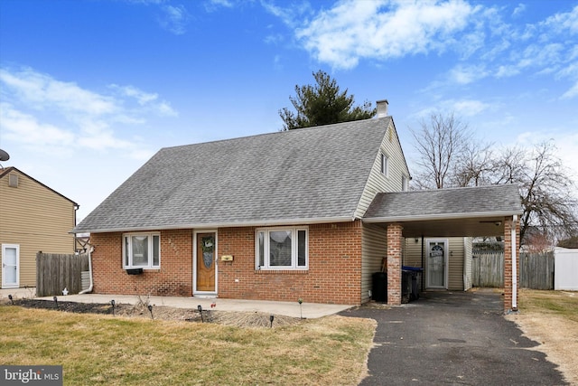 view of front of house featuring a shingled roof, fence, a carport, and brick siding