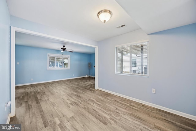 empty room with a ceiling fan, wood finished floors, visible vents, and baseboards