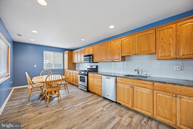 kitchen with visible vents, appliances with stainless steel finishes, dark stone countertops, light wood-style floors, and a sink