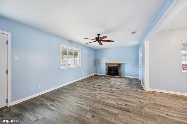 unfurnished living room featuring a brick fireplace, ceiling fan, baseboards, and wood finished floors