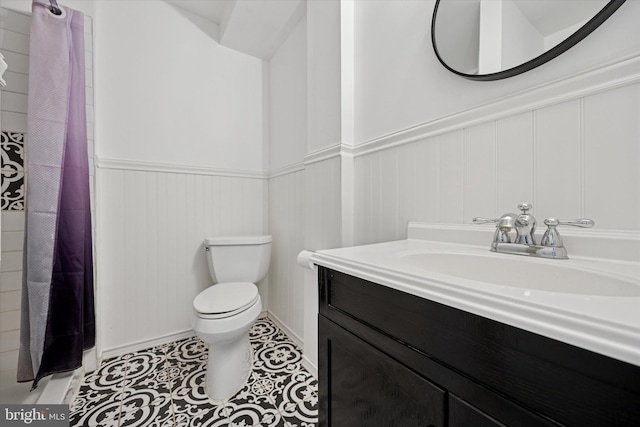 bathroom featuring toilet, a wainscoted wall, tile patterned floors, curtained shower, and vanity