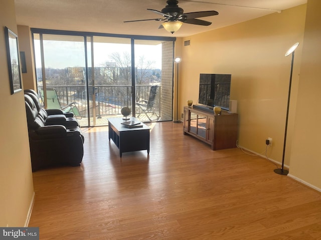 living room with a wall of windows, wood finished floors, visible vents, and baseboards