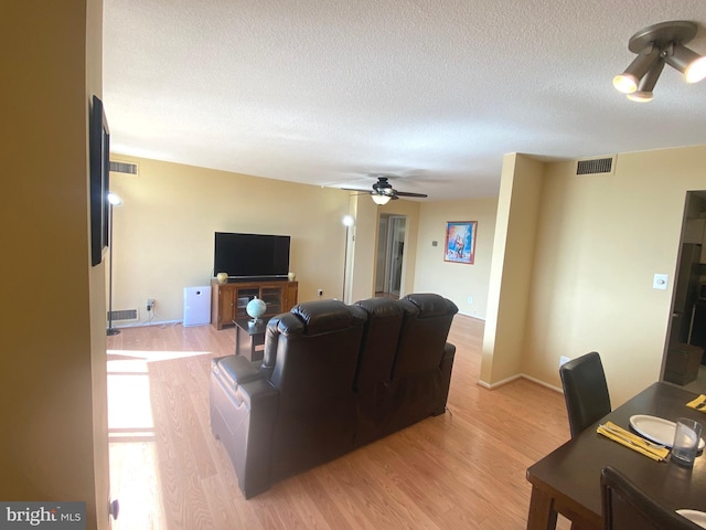 living area featuring light wood-type flooring, visible vents, ceiling fan, and a textured ceiling