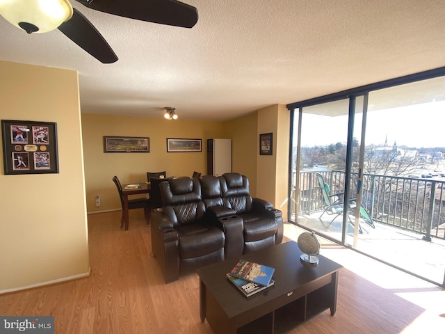 living room with baseboards, ceiling fan, expansive windows, a textured ceiling, and light wood-style floors